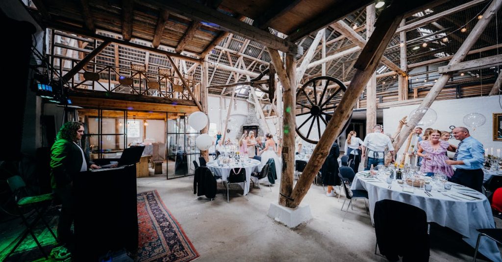 A vibrant wedding reception in a rustic barn setting with guests and a DJ.