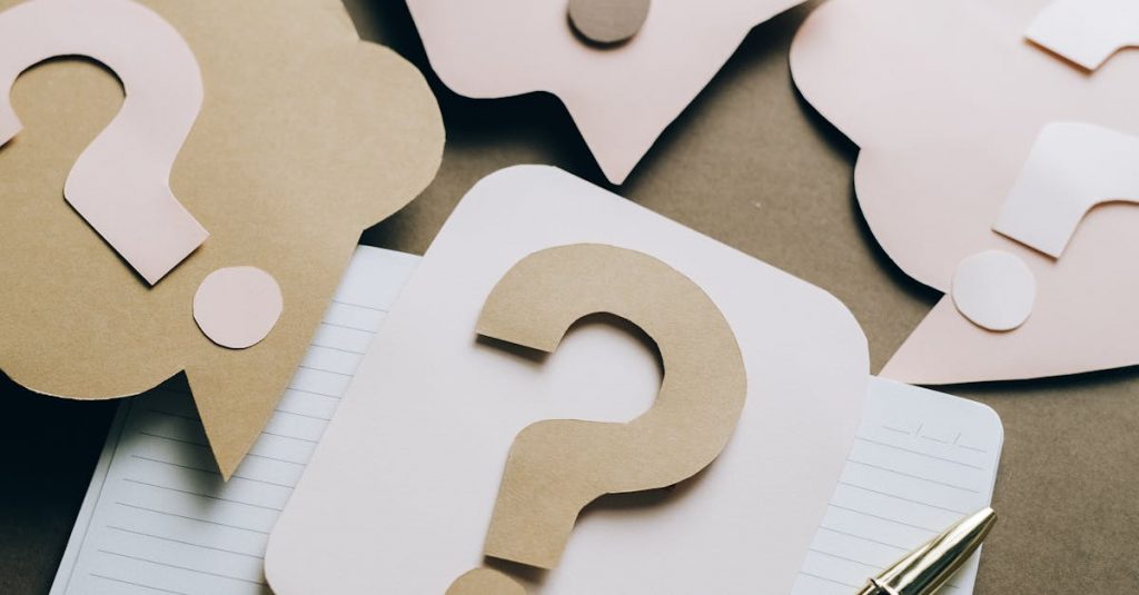 Artistic paper question marks on an open notebook with a pen, symbolizing curiosity and creativity.