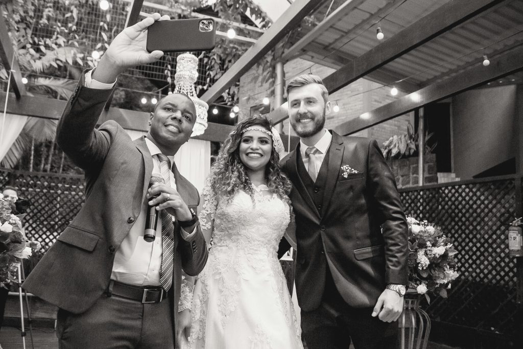 Black and white photo of a bride, groom, and officiant taking a joyful selfie at a wedding ceremony in Brazil.