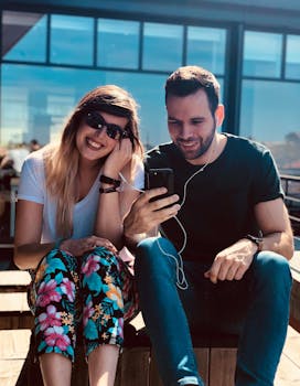 Smiling couple listening to music together with earphones, enjoying a sunny day outdoors.