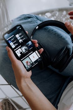 Close-up of a person holding a smartphone with headphones, browsing a music app.