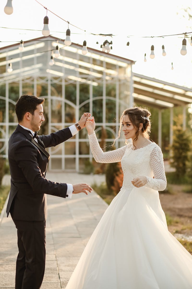 Bride and groom dancing outdoors in a sunlit garden, showcasing romance and elegance.