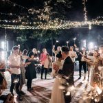 A couple dances under twinkling lights at a wedding reception, surrounded by guests holding sparklers.