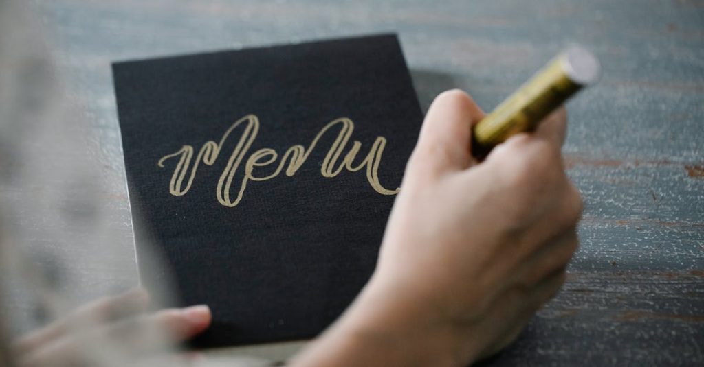 Close-up of a person writing 'Menu' in gold calligraphy on black cardstock with a gold marker.